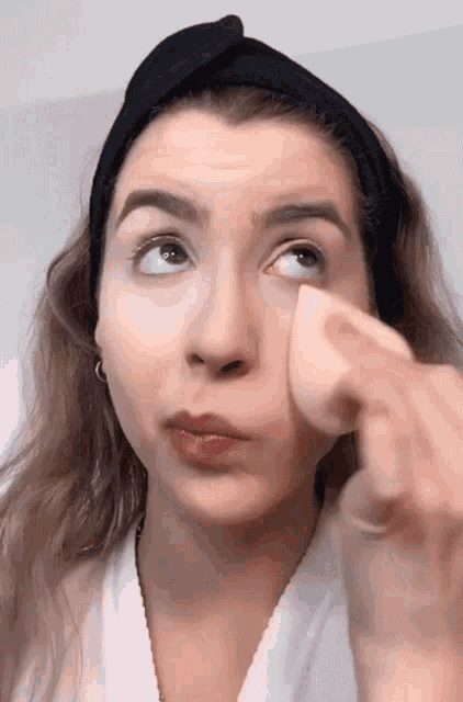 a woman wearing a black headband is applying makeup to her face