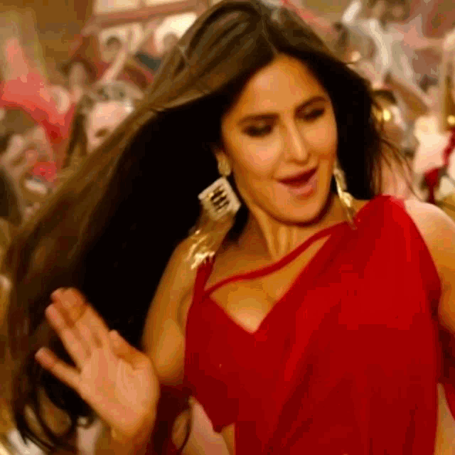 a woman in a red dress is dancing in front of a crowd while her hair is blowing in the wind .