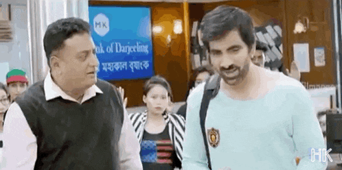 two men are standing next to each other in front of a bank of darjeeling sign .