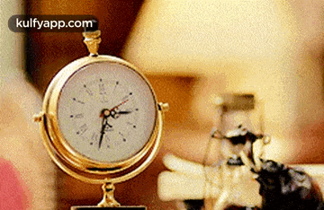 a gold clock is sitting on a table next to a lamp ..