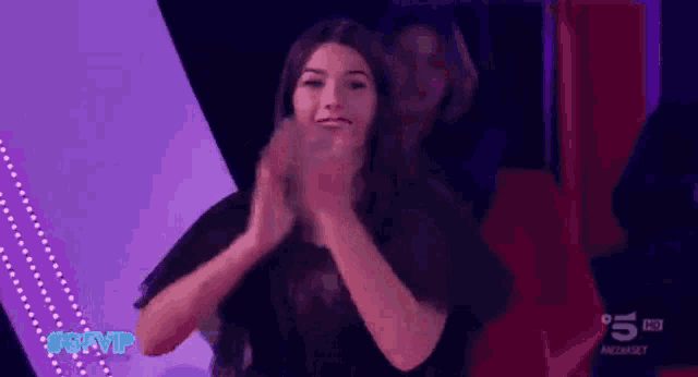 a woman applauds in front of a sign that says 5