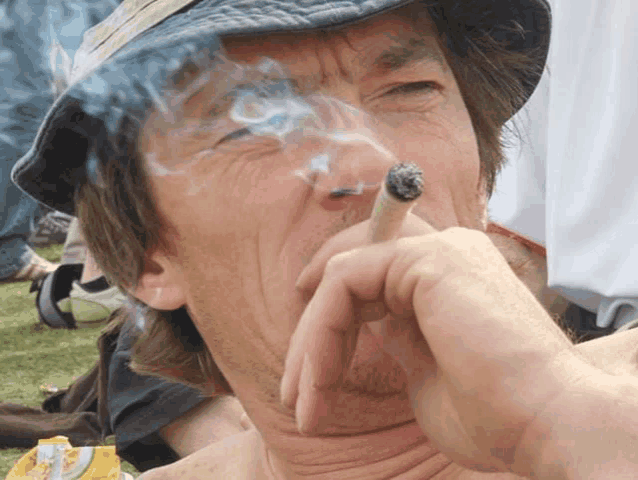 a man wearing a hat is smoking a cigarette with smoke coming out of his mouth