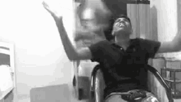 a man in a wheelchair is sitting with his arms outstretched in a black and white photo .