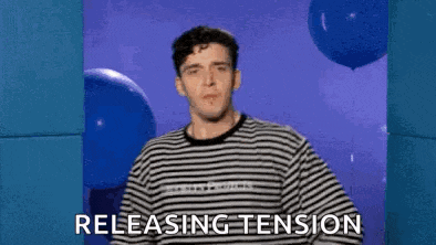 a man in a striped shirt is standing in front of blue balloons and saying `` releasing tension '' .