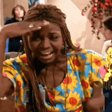 a woman wearing a floral shirt is smiling and covering her face with her hand