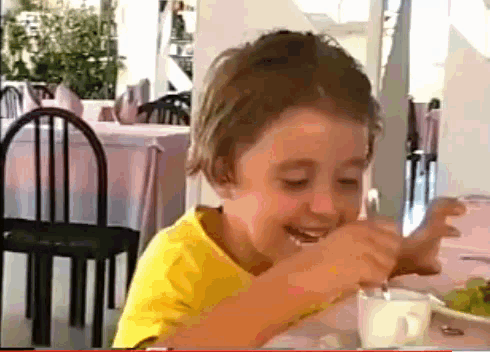 a young boy in a yellow shirt is sitting at a table in a restaurant