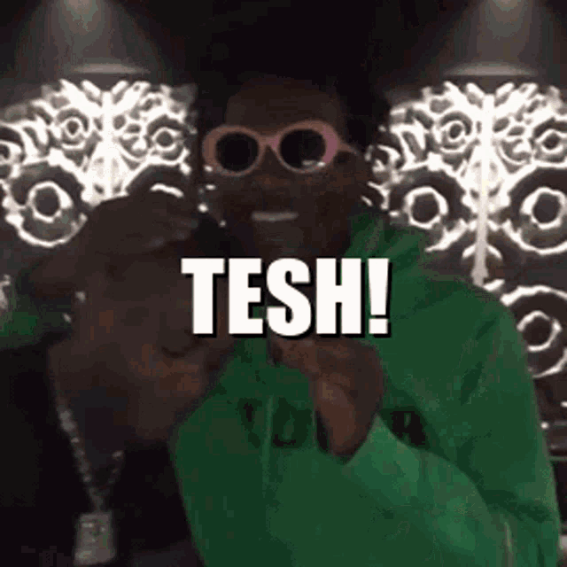 a man wearing pink sunglasses and a green hoodie says tesh
