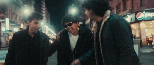 three men are walking down a street in front of a pepsi sign