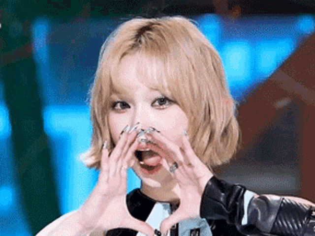 a young woman with blonde hair is making a heart shape with her hands .