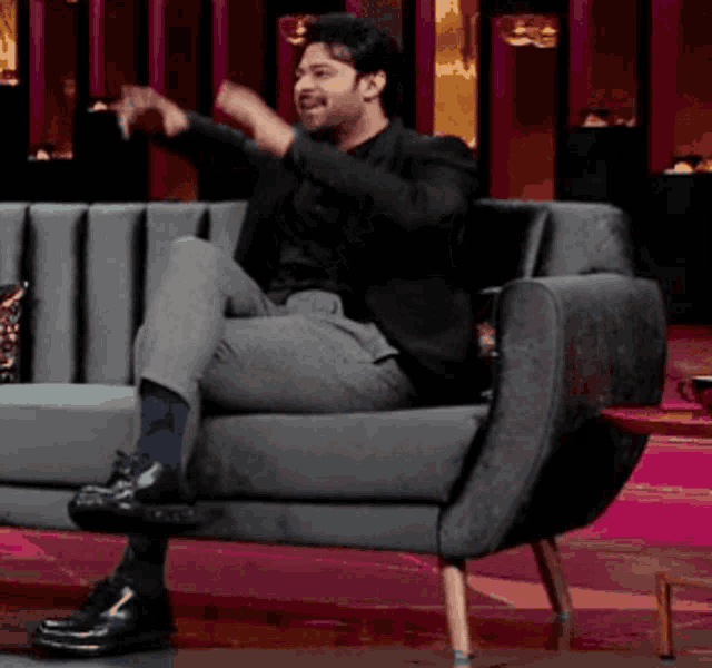 a man in a suit is sitting on a grey couch with his arms outstretched