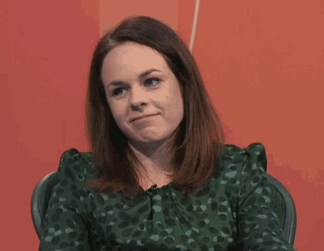 a woman wearing a green polka dot shirt is sitting in front of a red background