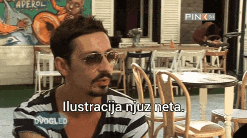 a man wearing sunglasses says ilustracija njuz neta while sitting at a table