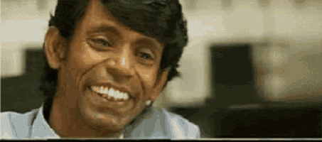 a man is smiling and looking at the camera while sitting in front of a laptop computer .