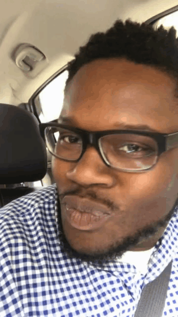 a man wearing glasses and a plaid shirt is sitting in the back seat of a car