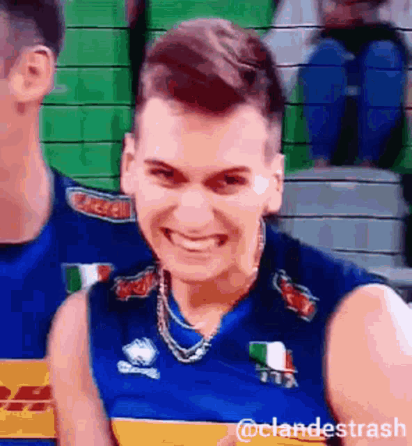 a man in a blue jersey is smiling and wearing a necklace