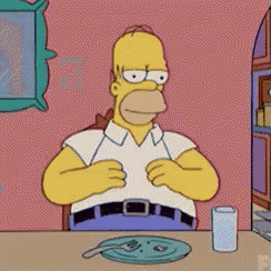 homer simpson is sitting at a table with a plate of food and a glass