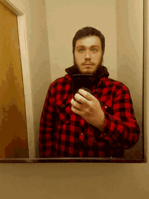 a man in a plaid shirt is taking a selfie in a bathroom mirror