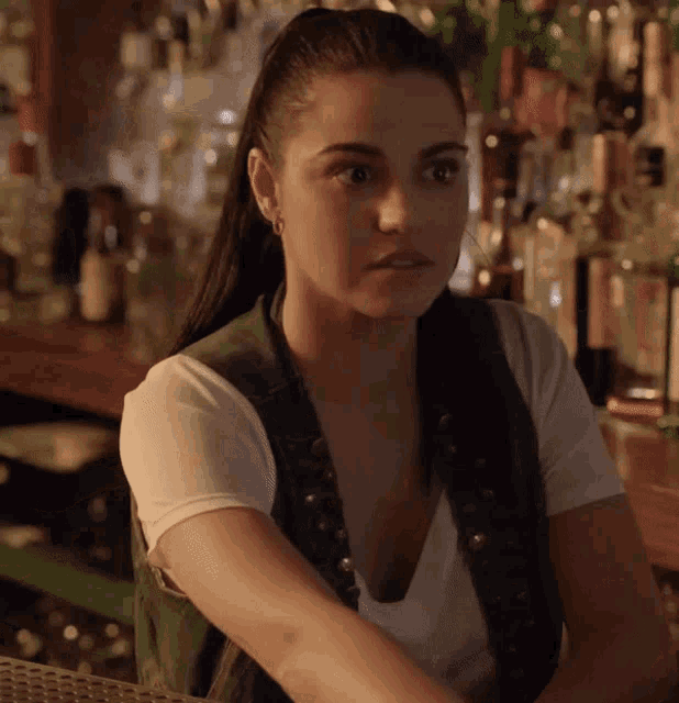 a woman is sitting at a bar with bottles of alcohol in the background