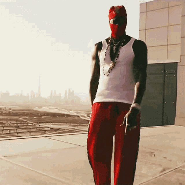 a man wearing a white tank top and red pants is standing on a rooftop