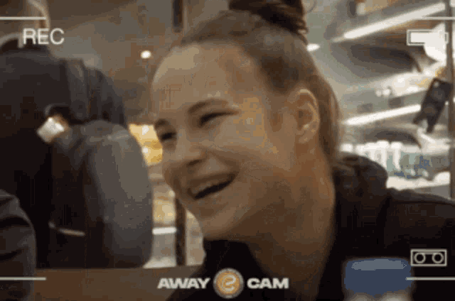 a woman is laughing in front of a camera that says away cam