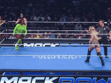 a woman in a green top is jumping in a wrestling ring with a mackbank sign in the background