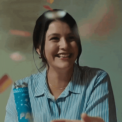 a woman in a striped shirt is smiling while holding a blue confetti cannon