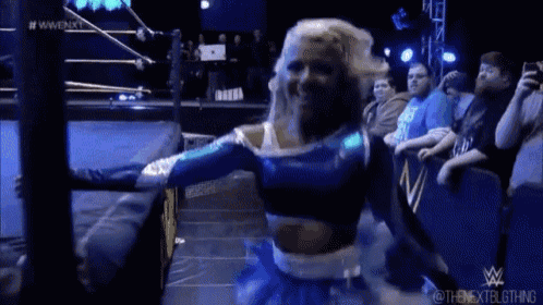 a woman in a blue and white dress is standing in a wrestling ring