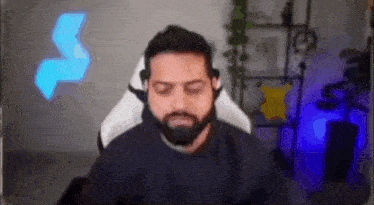 a man with a beard is sitting in a gaming chair with his eyes closed and headphones on .