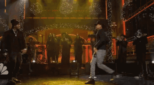 a man in a baseball cap is dancing on a stage with other people