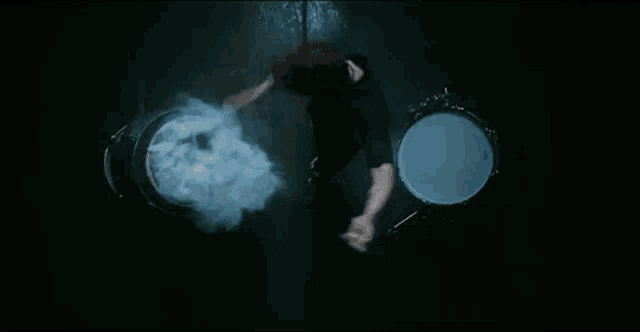 a person is playing a drum set in a dark room with smoke coming out of the drum set .