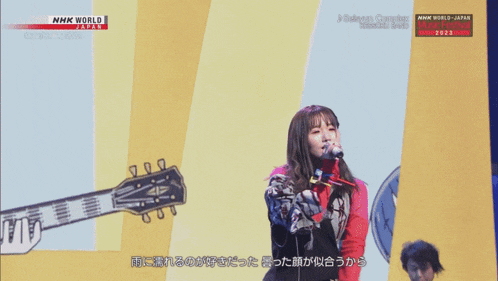 a woman singing into a microphone while holding a guitar in front of a nhk world logo