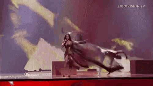 a woman is singing into a microphone on a stage while a bull is behind her .