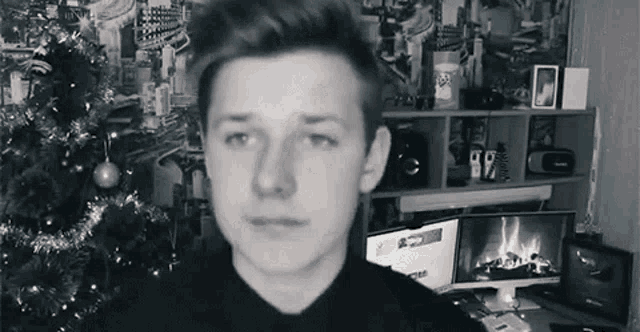 a black and white photo of a young man in front of a fireplace