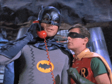a man in a batman costume talks on a telephone next to a man in a robin costume