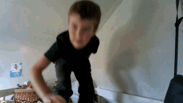 a young boy in a black shirt is jumping on a bed