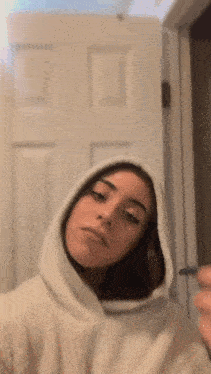a woman in a white hoodie is taking a selfie in front of a white door .