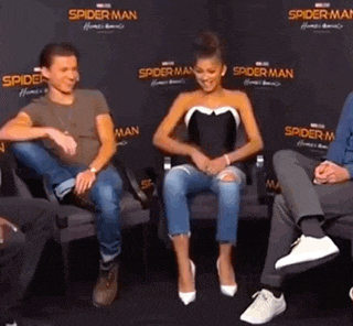 a group of people are sitting in chairs in front of a wall with spider man written on it .