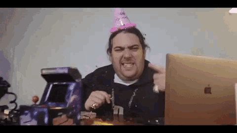 a man wearing a party hat is sitting at a table with a laptop .