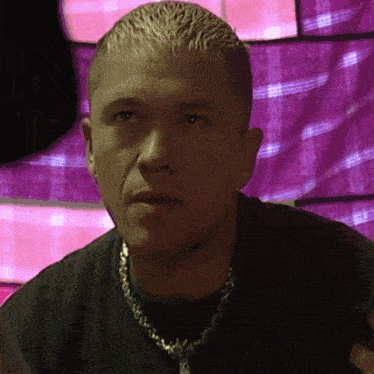 a man wearing a necklace and a black shirt looks at the camera