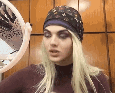 a woman wearing a bandana and a wig is looking in a mirror .