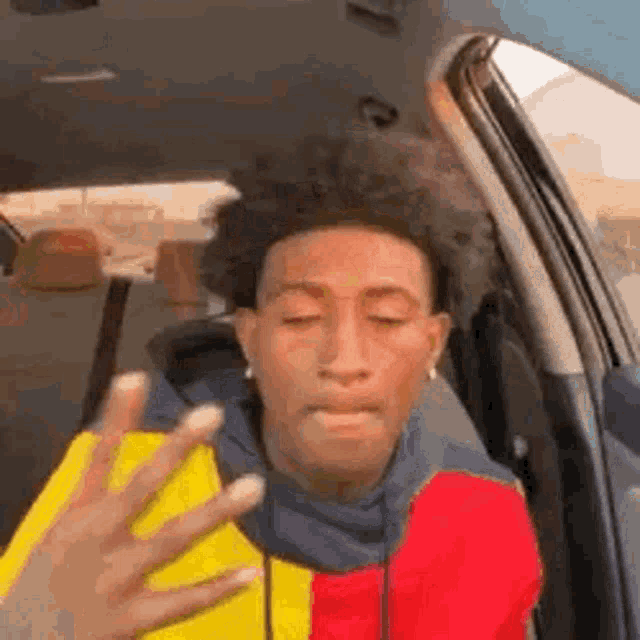 a man is sitting in the back seat of a car with his eyes closed and a hand reaching out towards him .