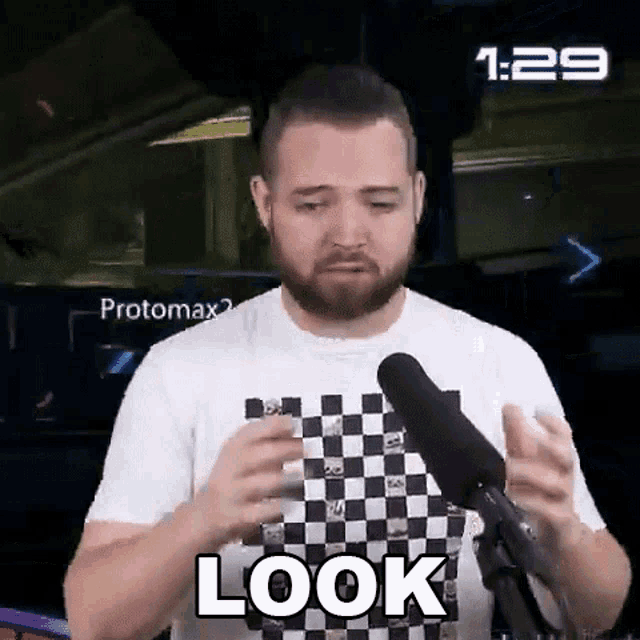 a man with a beard is standing in front of a microphone with the word look on his shirt .