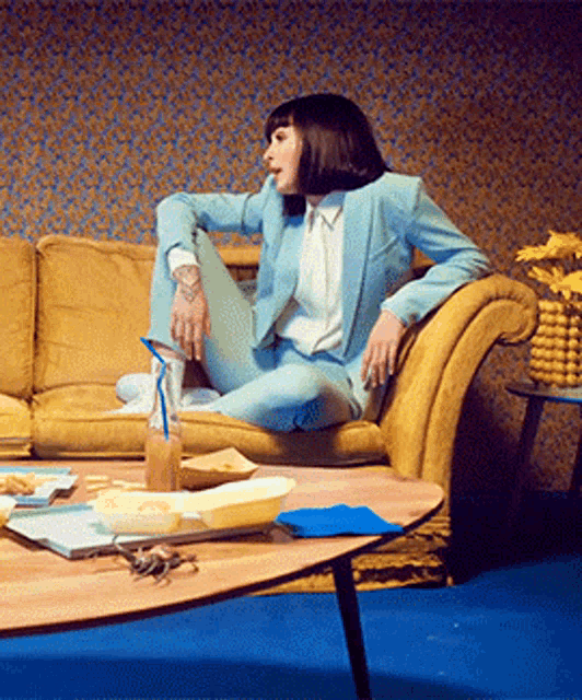a woman in a light blue suit sits on a yellow couch