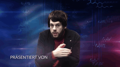 a man with a beard stands in front of a display of chemical formulas and the words präsentiert von
