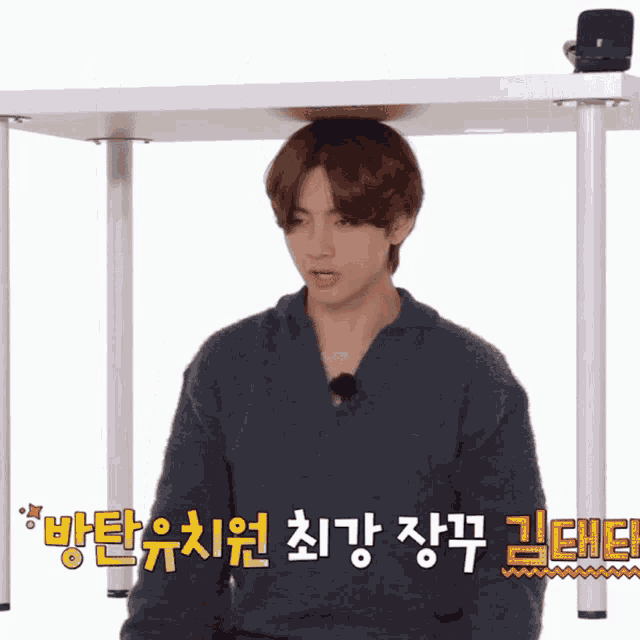 a man sitting under a table with korean writing on the bottom