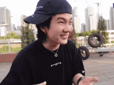 a young man wearing a hat and a necklace is smiling and making a funny face .