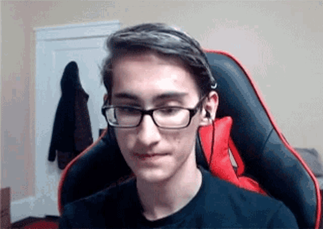 a young man wearing glasses and headphones is sitting in a black and red gaming chair .