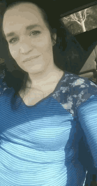 a woman is taking a selfie in a car while wearing a blue striped shirt .