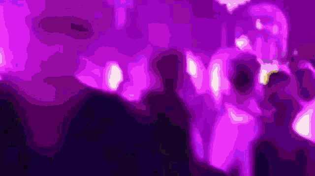 a group of people are dancing in a dark room with purple lights behind them .