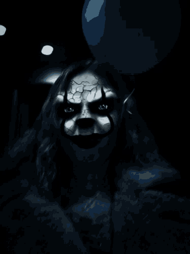 a scary clown with a blue balloon behind her